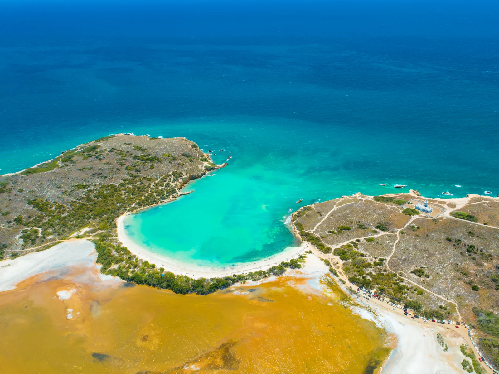 Aerial view of the beautiful Cabo Rojo with its famous lighthouse near the coast and a long line of parked cars, one of the best places to visit in Puerto Rico