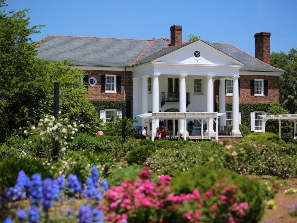 Three people taking shade near freshly painted huge white house at Boone Hall Plantation, one of the best South Carolina attractions with vibrant flowers