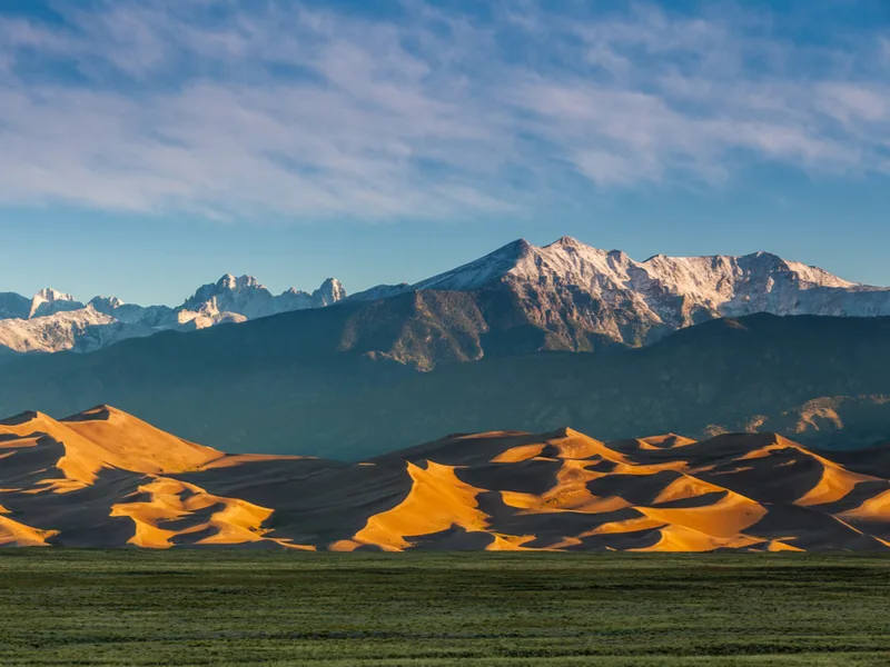 One of the best places to visit in Colorado, the Great Sand Dunes National Park and Preserve, as pictures with mountains in the background