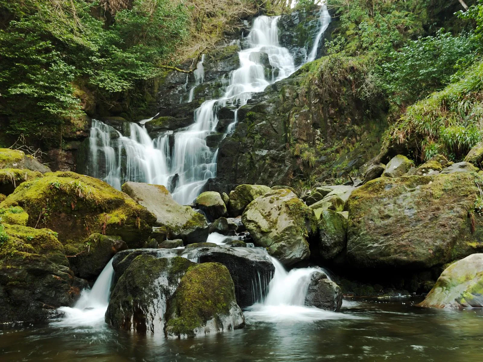 Moss-covered boulders at the calm Torc Waterfall in Killarney, a piece of the best places to visit in Ireland