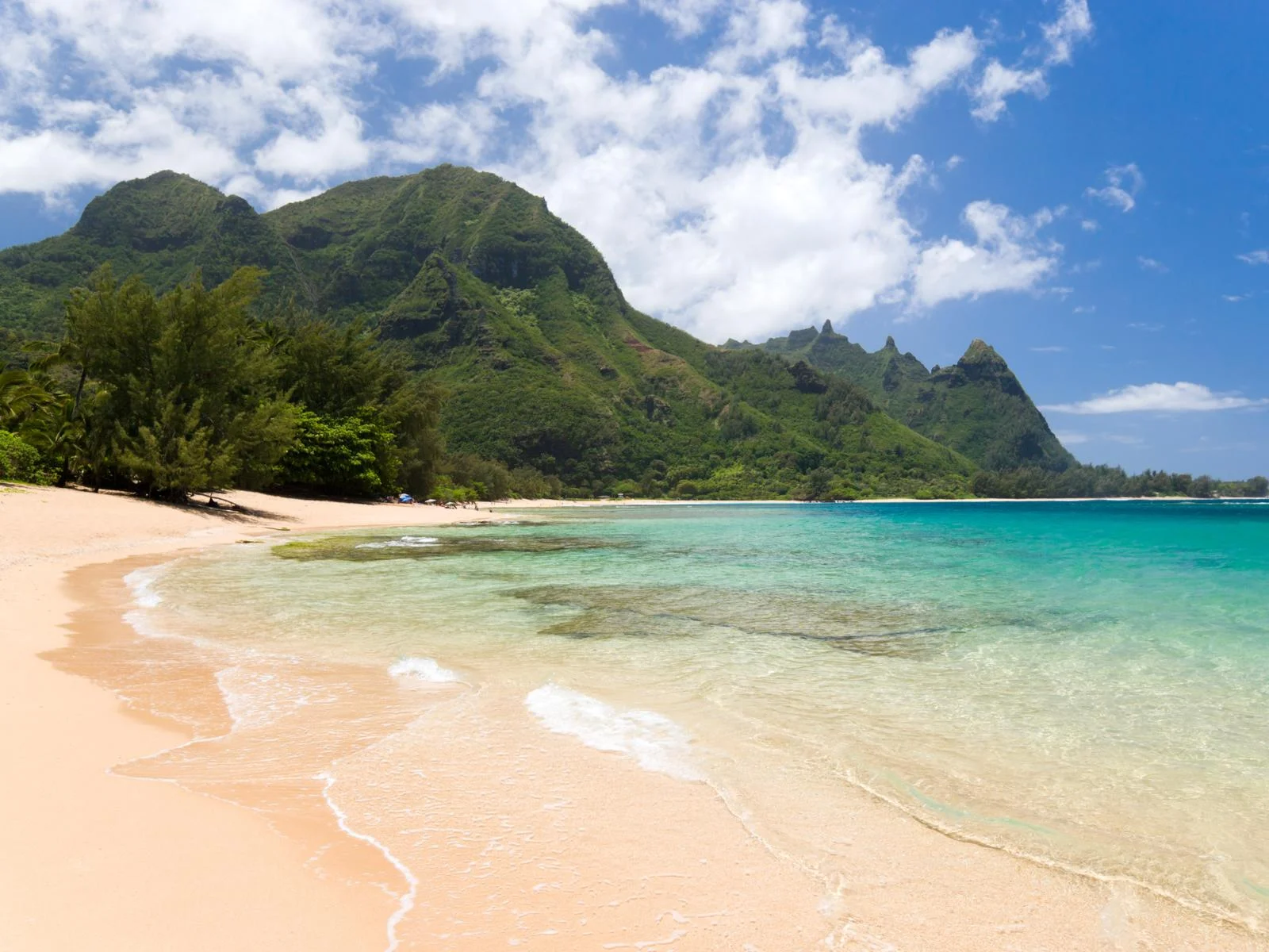 Fine sand at the secluded Haena Beach with a unique mountain formation covered with trees, one of the best beaches in Kauai