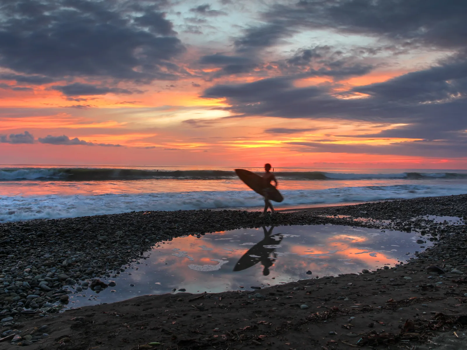 Silhouette of a running surfer and tall waves on a lovely sunset at the rocky shore of Dominical Beach, one of the best beaches in Costa Rica