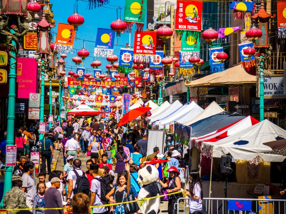 People of various races enjoying the busy day at Chinatown, one of the best places to visit in San Francisco, for the Autumn Moon Festival with tents and vibrant red all over the place