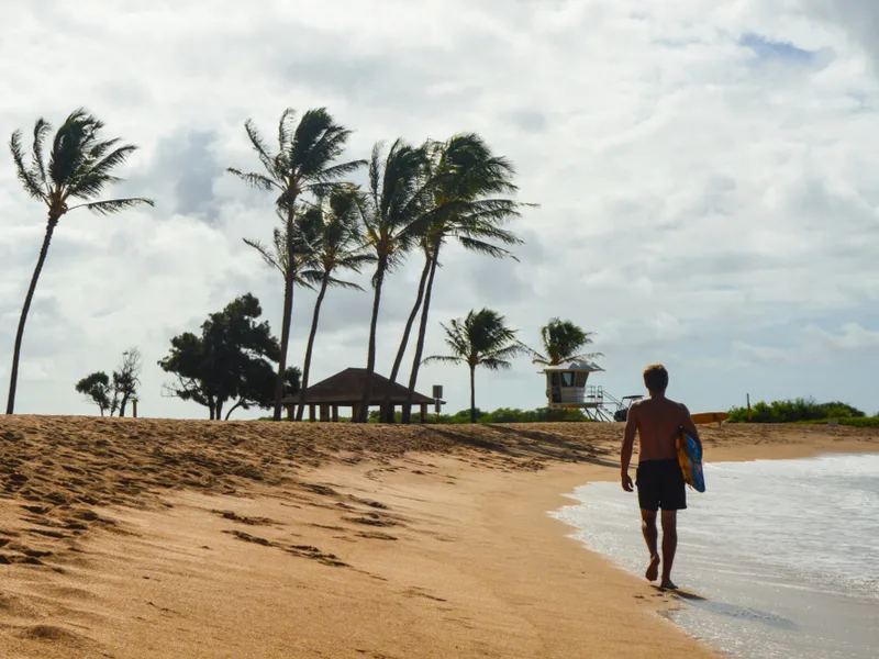 Surfer walking along Salt Pond Beach in Kauai, one of the best beaches in Hawaii