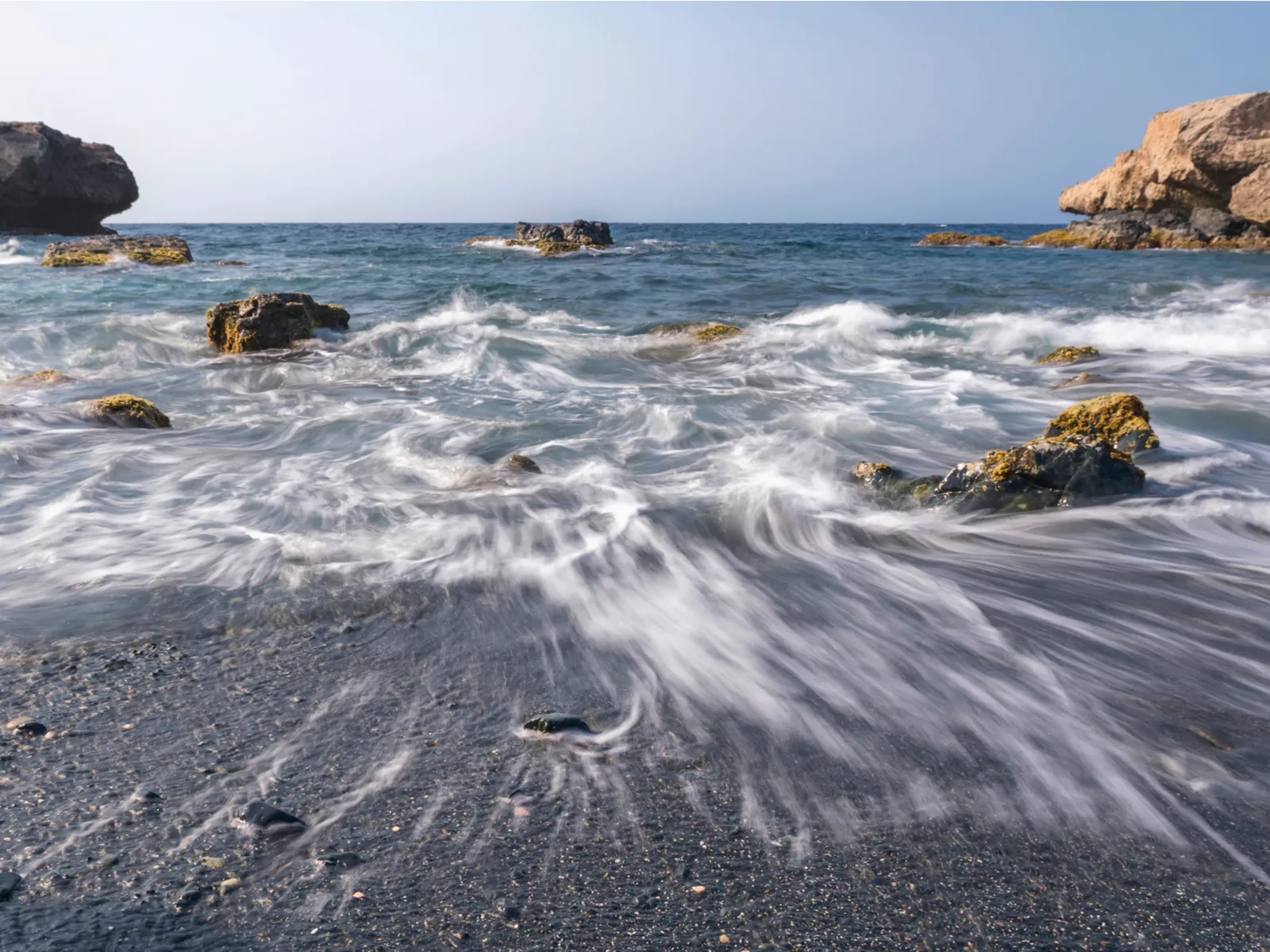 High exposure photo of waves at Blackstone Beach, one of the best beaches in Aruba, with its distinct black sand and some huge rocks offshore