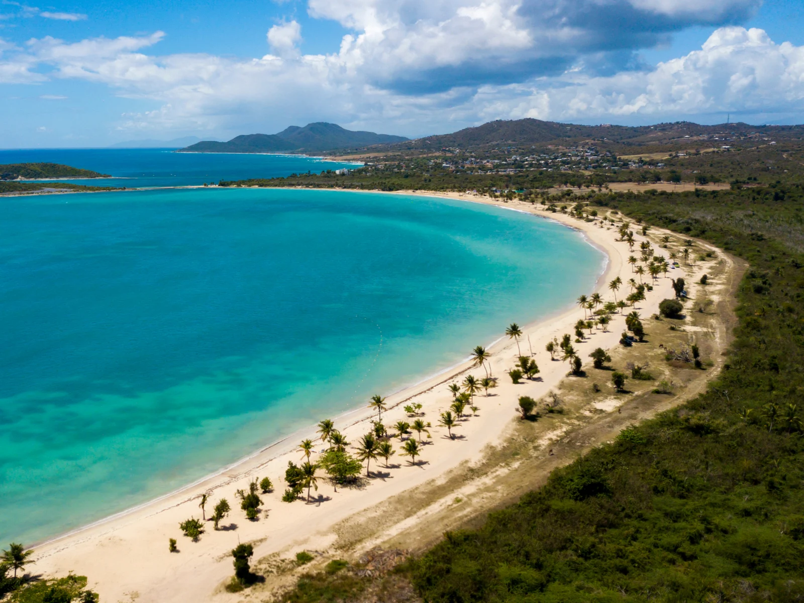 Aerial view of Sun Bay Beach, one of the best beaches in Puerto Rico, with teal water and green vegetation on the other side on a semi-sunny day