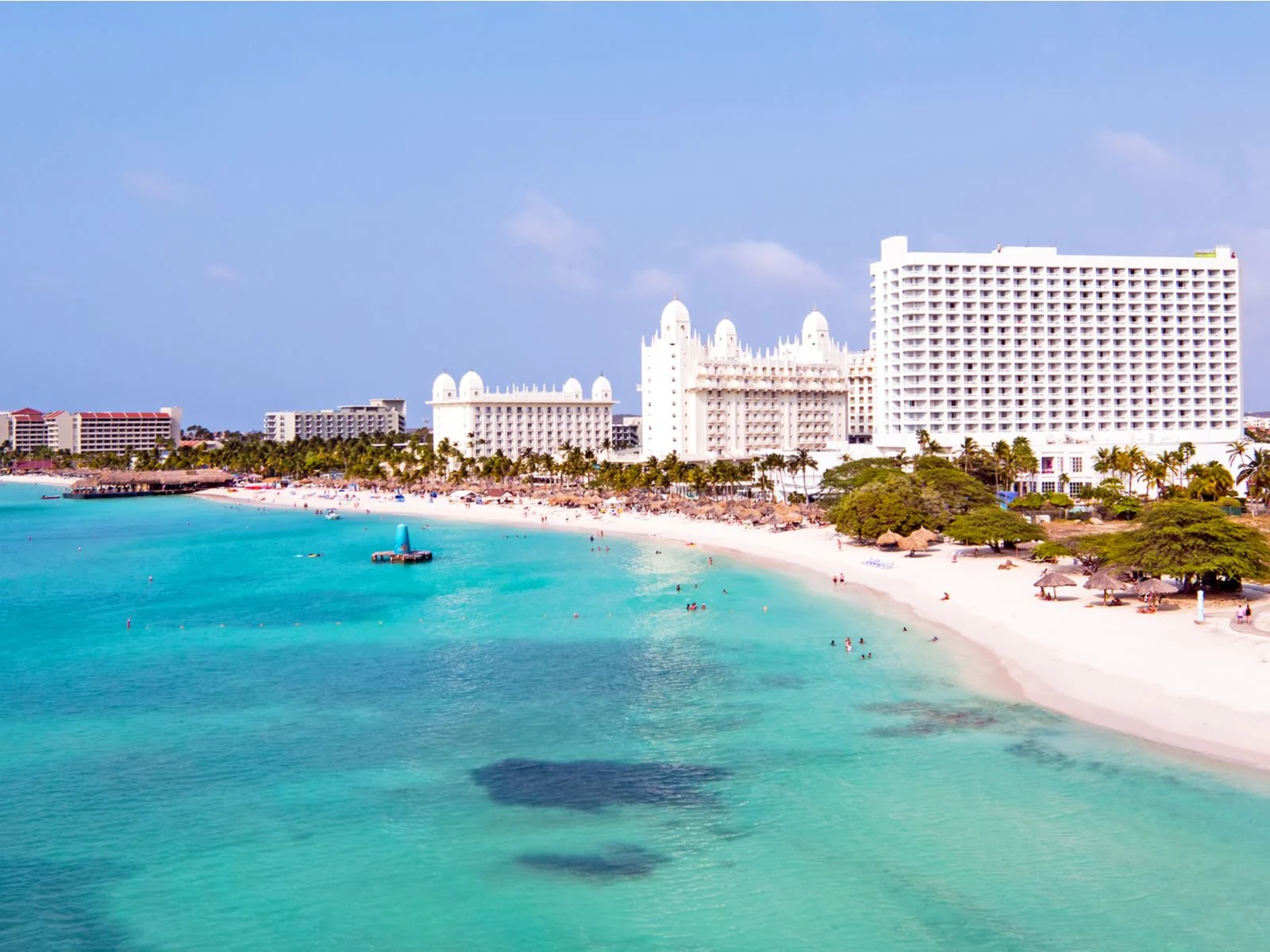 Aerial view on the long stretch of bright white sand and crisp clear blue waters of Palm Beach, one of the best beaches in Aruba, and lovely people enjoying the bright day at the beach