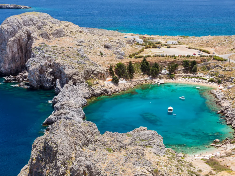 Rocks engulfing a portion of the turquoise sea with two anchored boats at St Paul's Bay on Lindos in the Island of Rhodes, one of the best places to visit in Greece