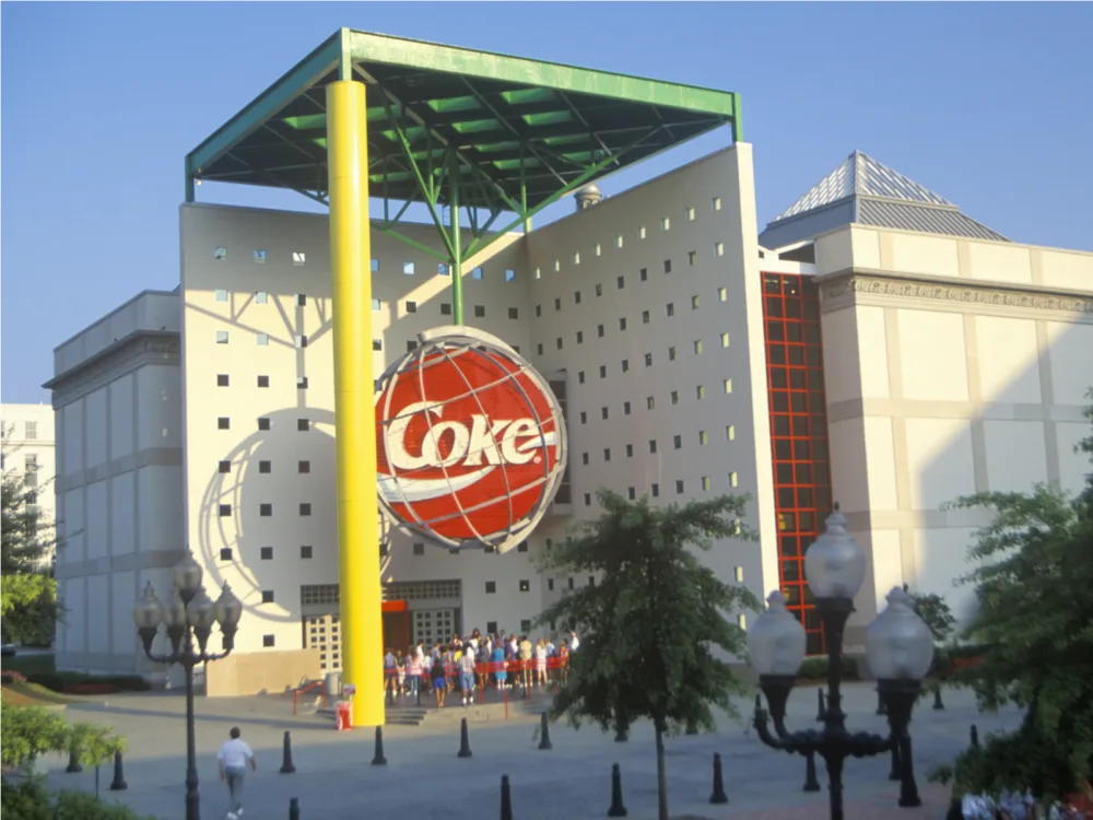 Tourists standing below a gigantic Coke icon inside a globe at World of Coca Cola as one of the best tourist attractions in Georgia, casting a sharp shadow in the late afternoon